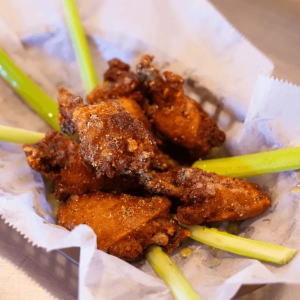 Crispy fried chicken wings with seasoning and celery sticks in a paper-lined basket.