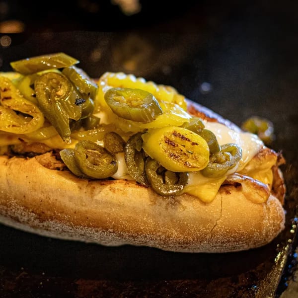 A JD's Cafe southern sandwich with melted cheese, grilled peppers, and jalapeños on a dark surface.