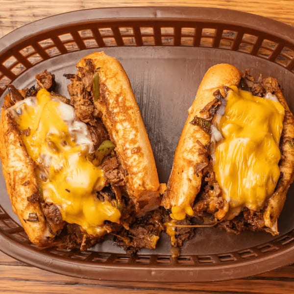 Two cheesy steak and pepper subs in a brown basket from JD's Cafe.