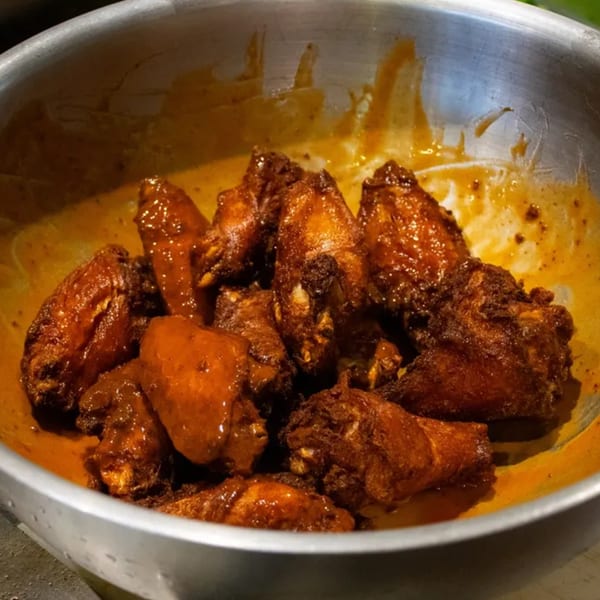 JD's Cafe's southern-style chicken wings, coated in a rich, glistening orange sauce, in a metal bowl.