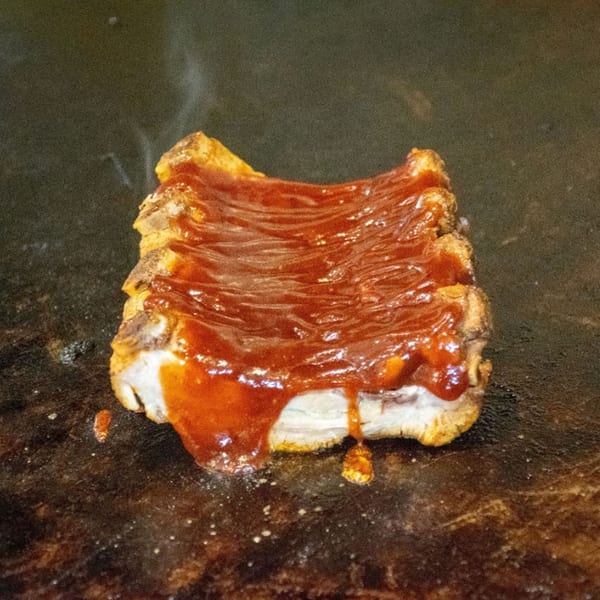 Southern-style ribs with barbecue sauce sizzling on a dark grill, smoke rising.